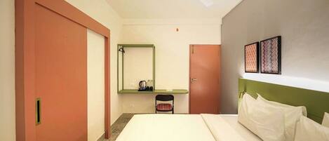 Une chambre d’hôtel comprenant un lit, une chaise, un bureau avec un miroir, un ventilateur de plafond et deux tableaux encadrés accrochés au mur.
