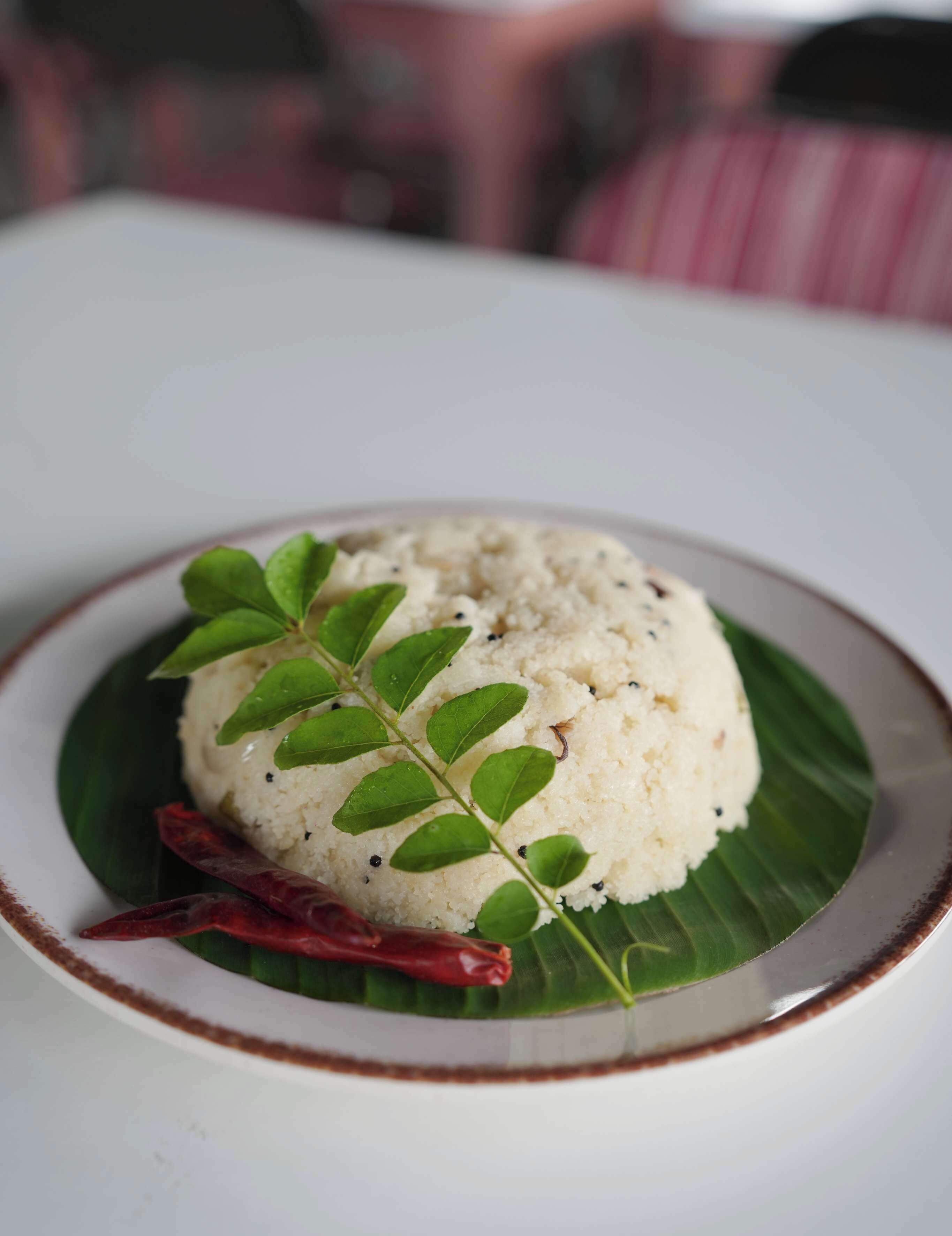 A plate of idli with a green leaf garnish on a white plate with a brown rim.