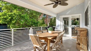 Un patio cubierto con una mesa y sillas, un ventilador de techo y vistas de vegetación exuberante.