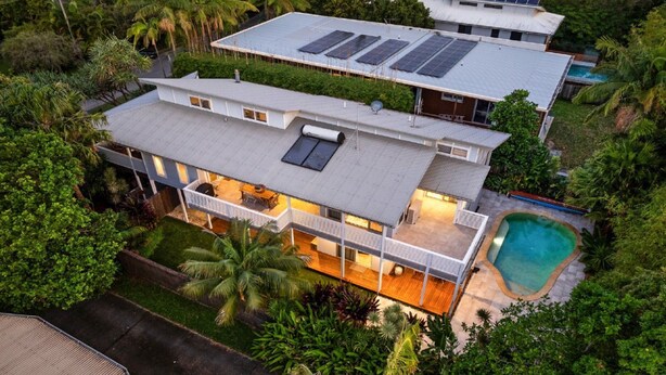 Una casa de dos pisos con un sistema de paneles solares en el techo, una piscina y un jardín bien cuidado.