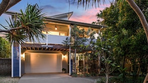 A modern two-story house with a garage, surrounded by lush greenery and a clear sky. - The Anchorage - by Lifestyle. Brunswick Heads (NEW BRIGHTON)