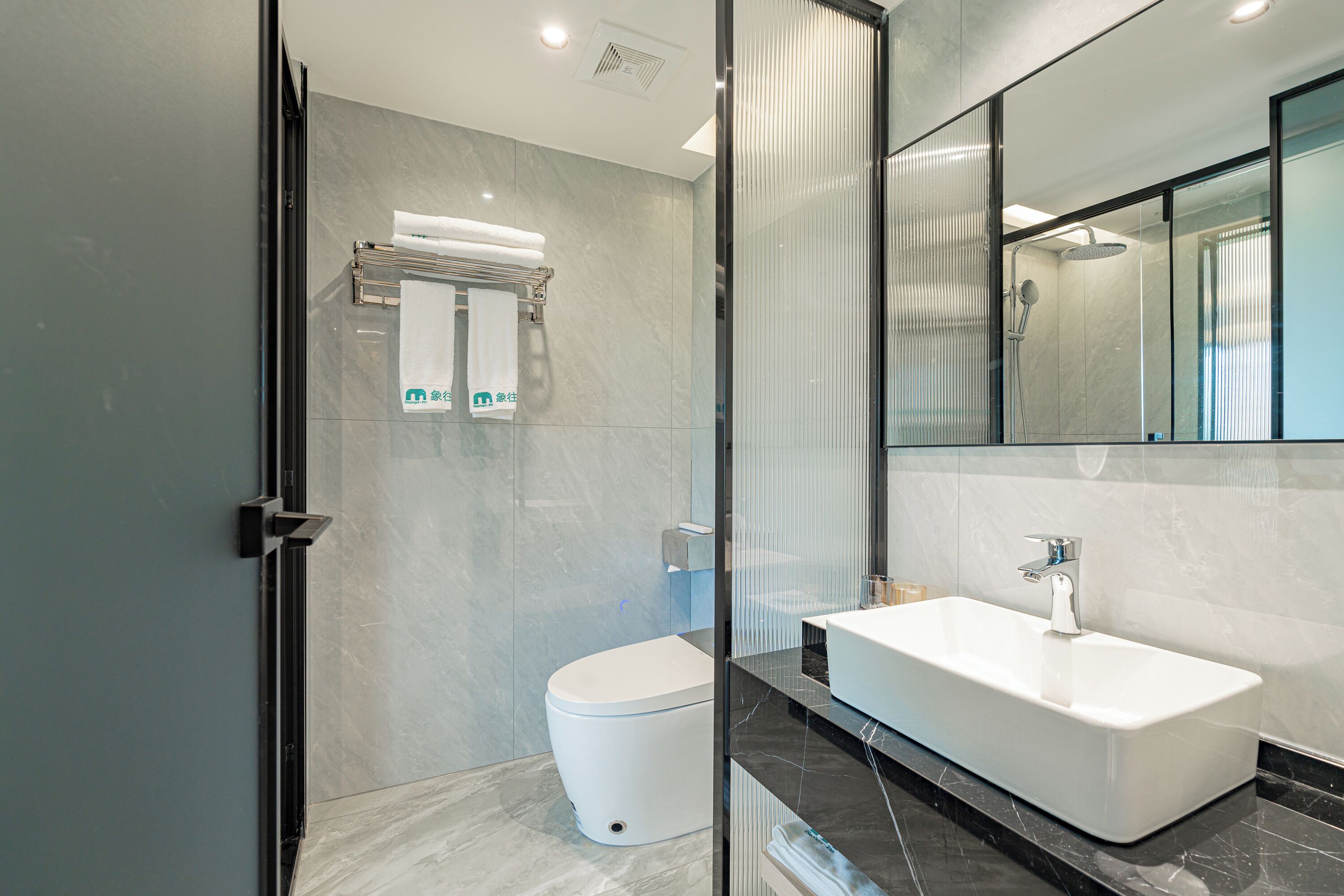 A modern bathroom with a glass shower enclosure, a white toilet, and a large rectangular sink with a mirror above it.
