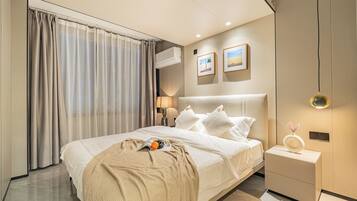 A modern hotel room with a large bed, a bedside table, a nightstand, and a wall-mounted air conditioner.