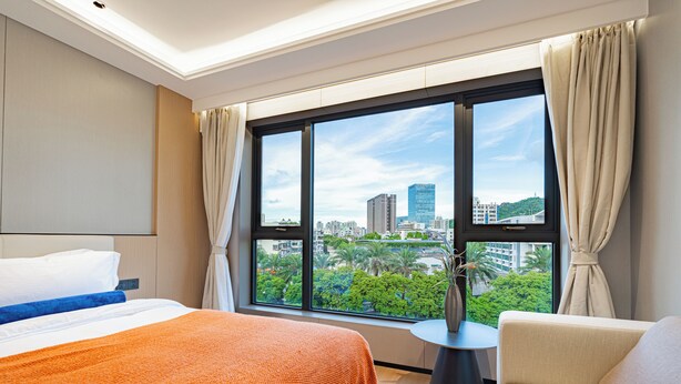 A hotel room with a large window, a bed, a chair, and a small table. - Xiangwang Meisu Hotel (Zhuhai)