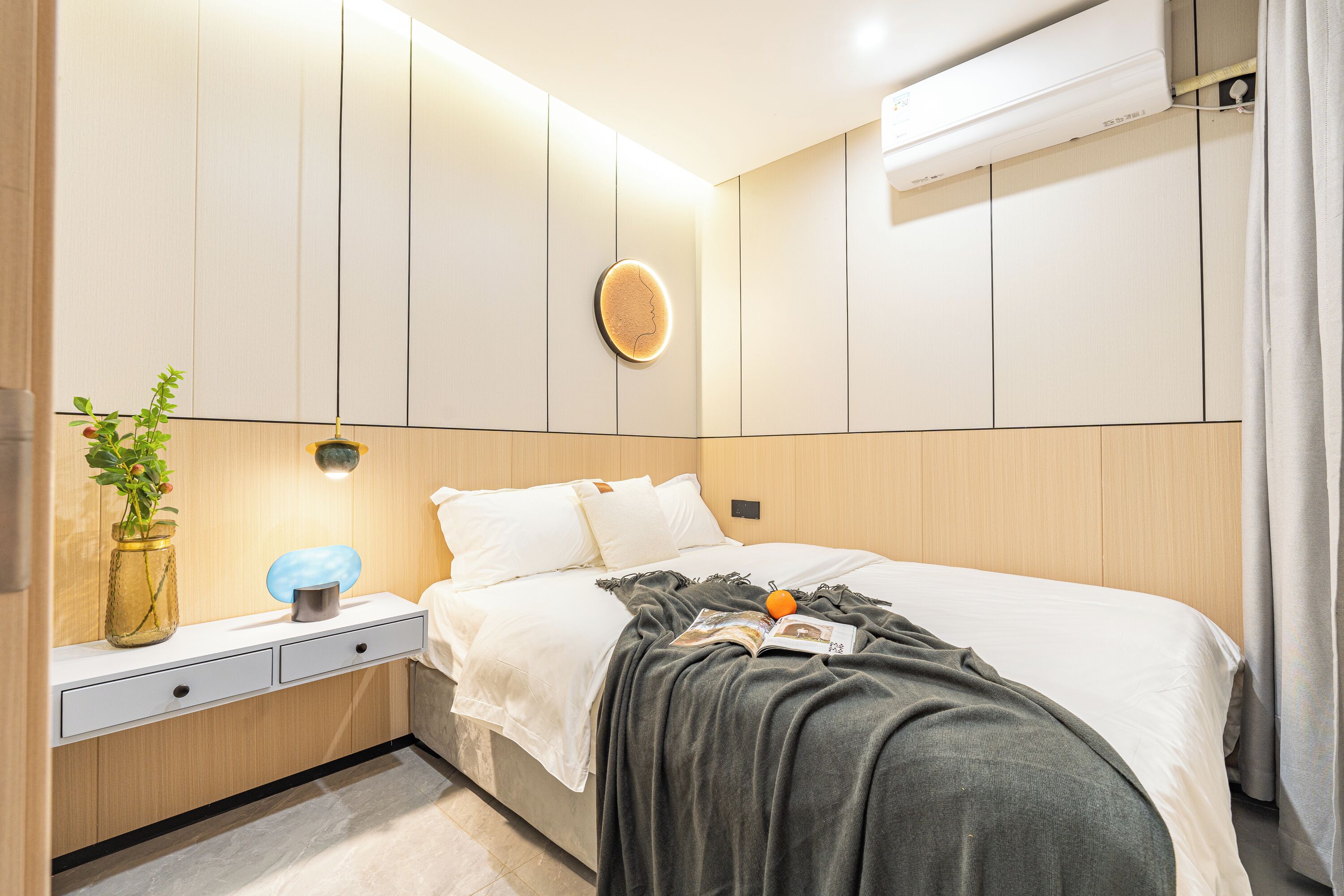 A modern bedroom with a bed, bedside table, and a wall-mounted light fixture.