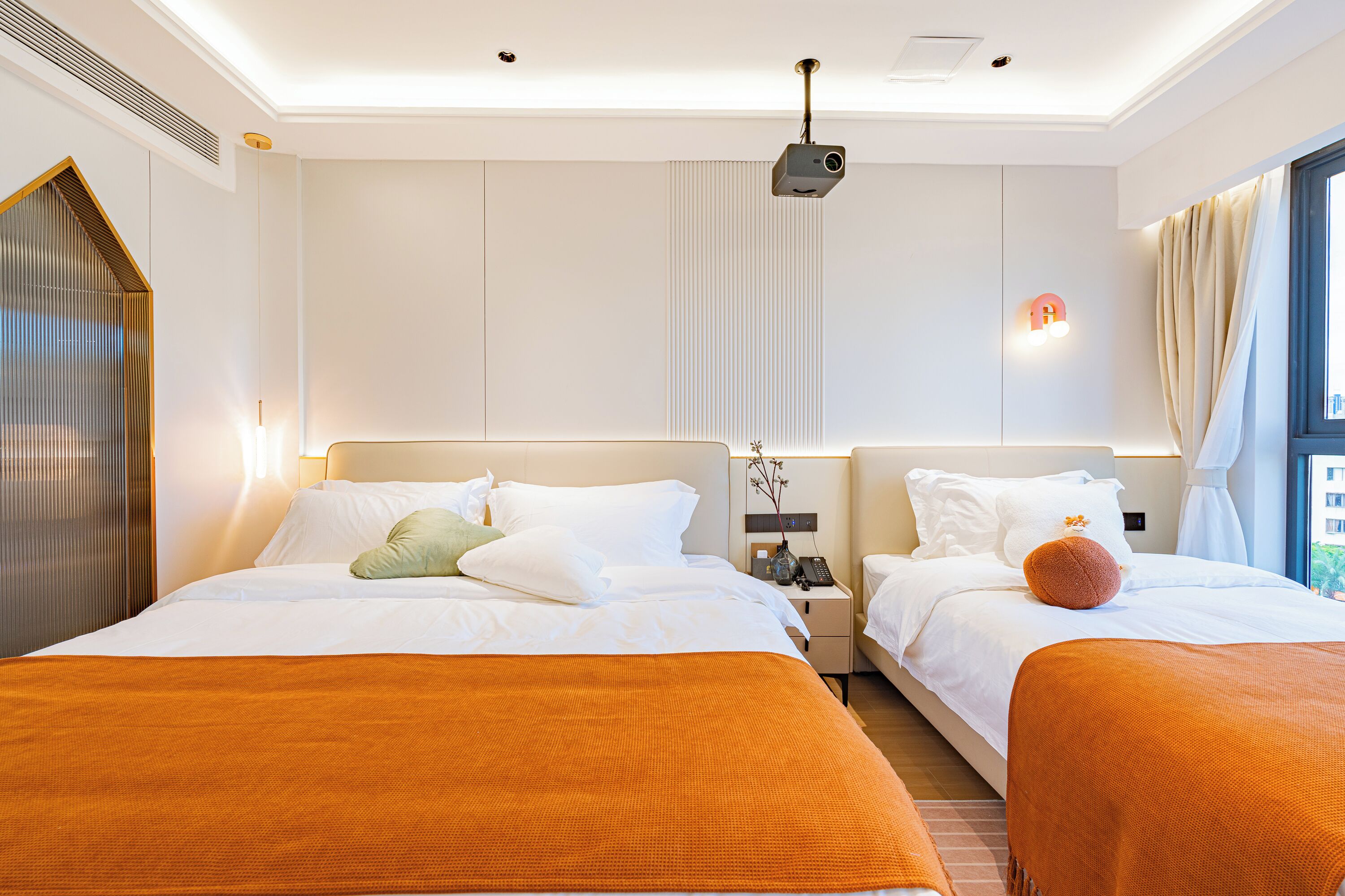 Habitación de hotel con dos camas, un proyector, una mesita de noche y una ventana con cortinas.