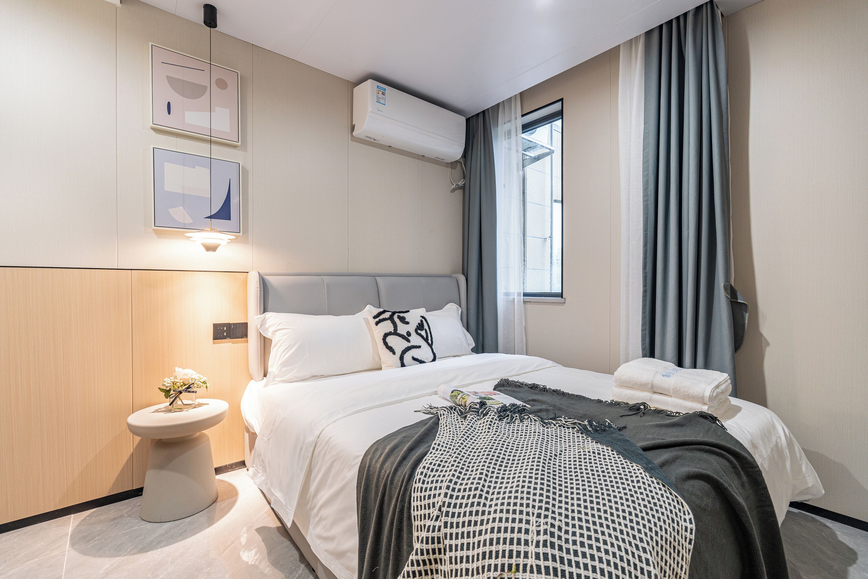 Una habitación de hotel moderna con cama, mesita de noche y ventana con cortinas.