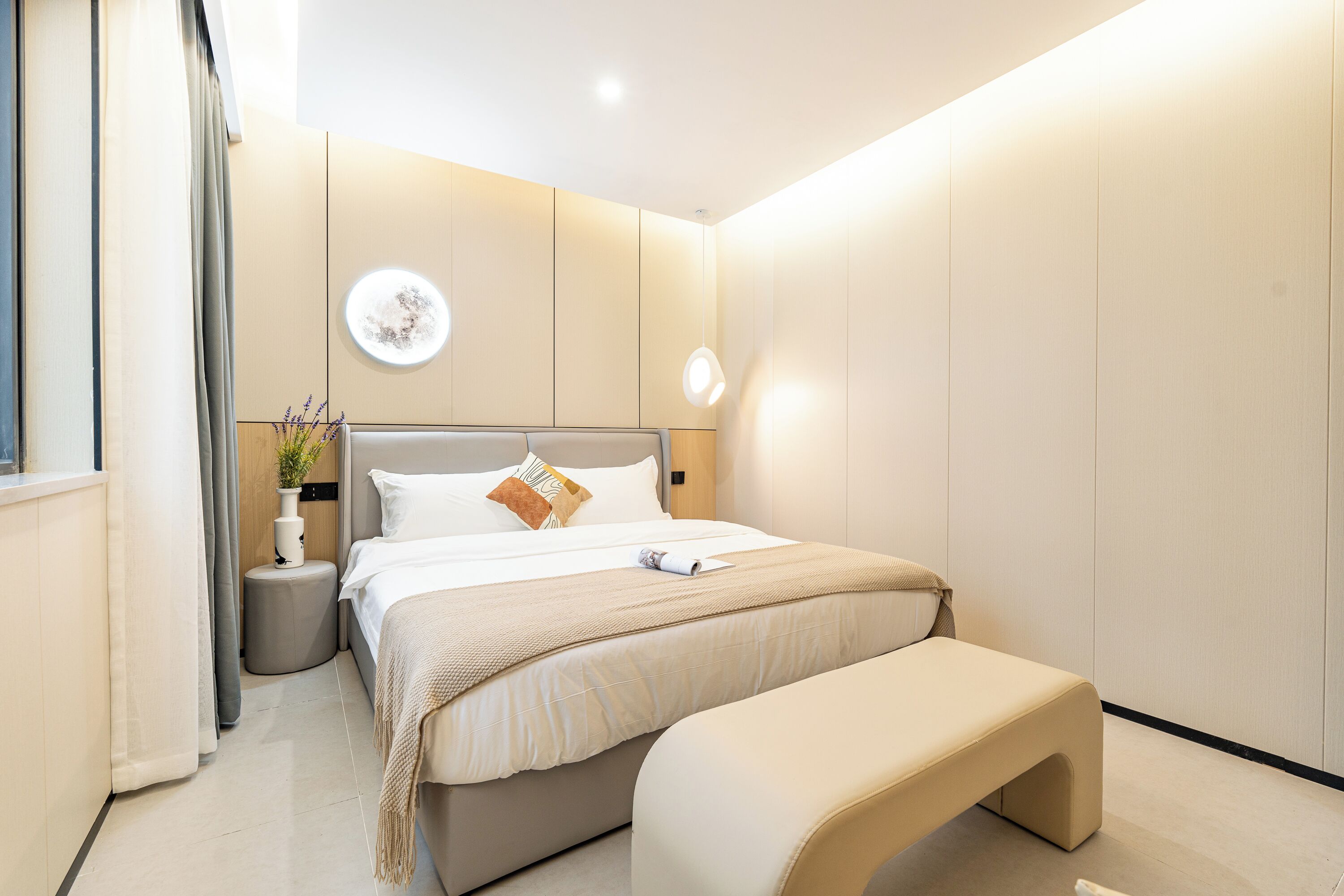 Un dormitorio moderno con una cama grande, mesitas de noche, una lámpara de pared y una pequeña planta en maceta.