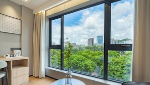 A modern room with a large window, a desk, a chair, and a small table with a vase. - Xiangwang Meisu Hotel (Zhuhai)