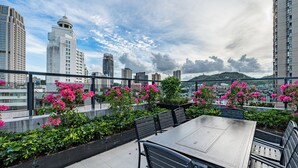 A rooftop terrace with a dining table and chairs, surrounded by lush greenery and pink flowers. - Xiangwang Meisu Hotel (Zhuhai)