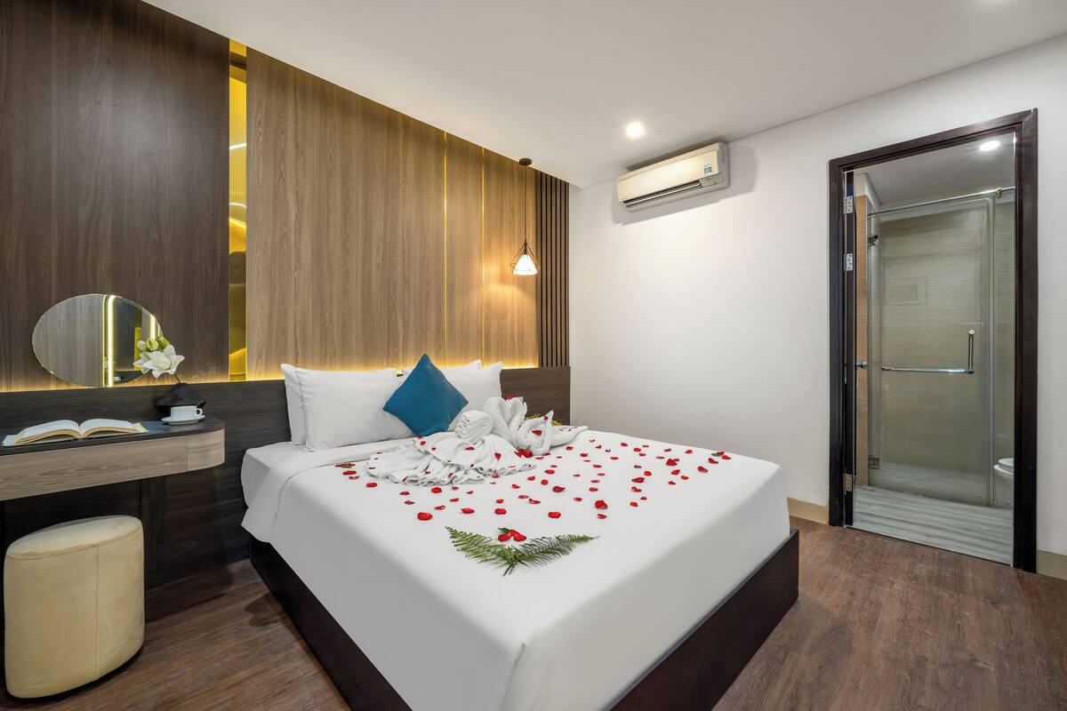 Une chambre d’hôtel moderne avec un grand lit, une table de chevet avec un livre et une tasse, un miroir et un espace douche.