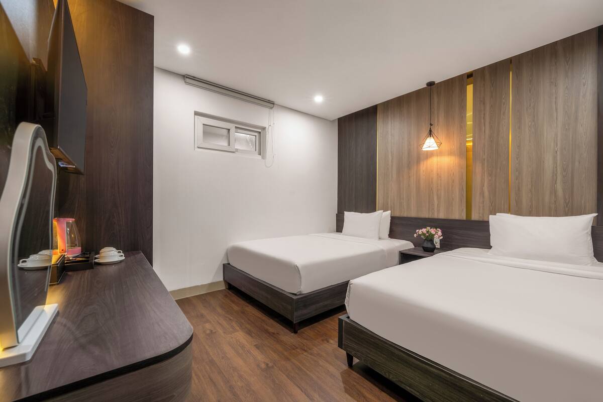 Une chambre d’hôtel avec deux lits, un bureau, un miroir et un luminaire fixé au mur.