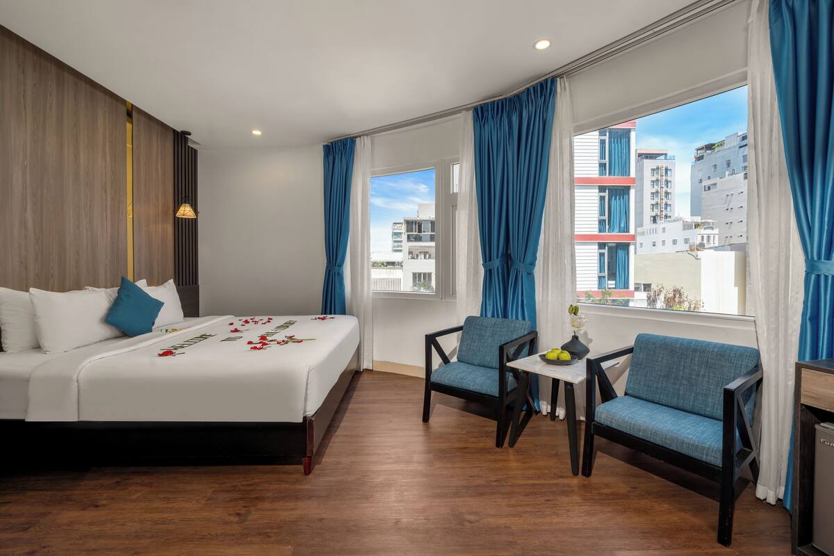 Une chambre d’hôtel avec un lit, deux chaises, une petite table et une fenêtre avec des rideaux.