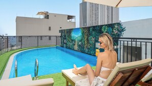 Zona de piscina con un mural, una silla de descanso y un rascacielos al fondo.