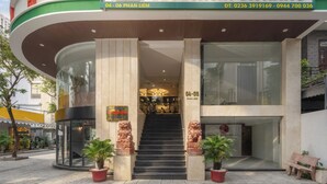 Entrada de hotel con diseño moderno, que presenta una fachada curva, puertas de vidrio y una escalera que conduce al vestíbulo.
