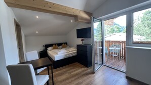 Ein Schlafzimmer mit Bett, Nachttisch, Fernseher und Blick auf einen Balkon mit Gartenmöbeln.