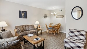 A living room with a sofa, armchair, coffee table, and dining table with chairs.
