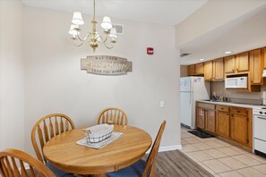 A dining area with a wooden table and chairs, a chandelier, and a kitchen with wooden cabinets and white appliances.