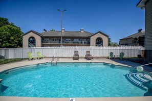 A swimming pool with a 4 FT depth marker, surrounded by lounge chairs and a white fence.