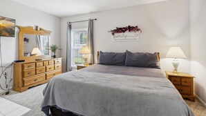 A bedroom with a bed, wooden dresser, bedside lamps, a mirror, and a wall decoration.