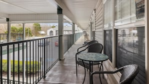 A covered outdoor area with a row of wicker chairs and a table, a railing, and a view of the street.
