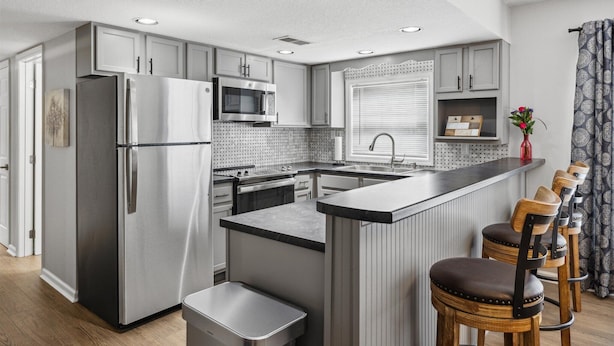 A modern kitchen with stainless steel appliances, a central island with bar stools, and a window with blinds.