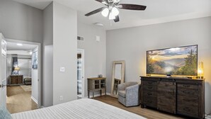 A bedroom with a large bed, a dresser, a chair, a ceiling fan, and a painting on the wall.