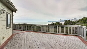 Een houten terras met een reling, met uitzicht op water en verre bergen.