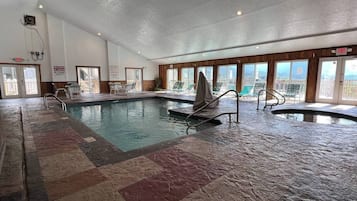 An indoor swimming pool with multiple lanes, a lifeguard chair, and a view of the city through large windows.