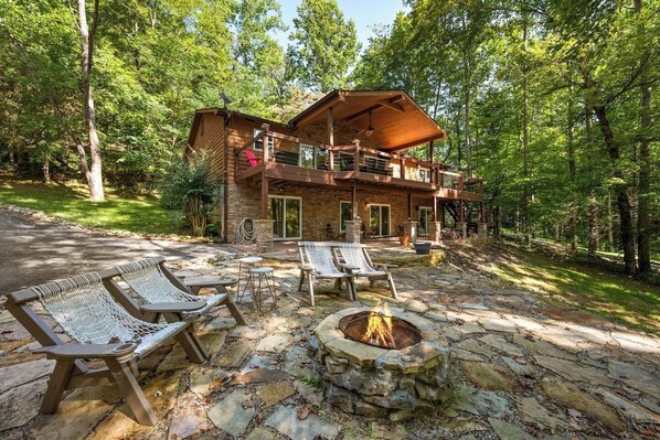 Una cabaña con un hogar de piedra, mobiliario exterior y una terraza con vistas a un bosque.