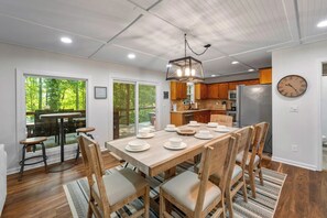 Un comedor con una mesa y sillas de madera, una lámpara de araña y vistas al exterior a través de puertas de vidrio.