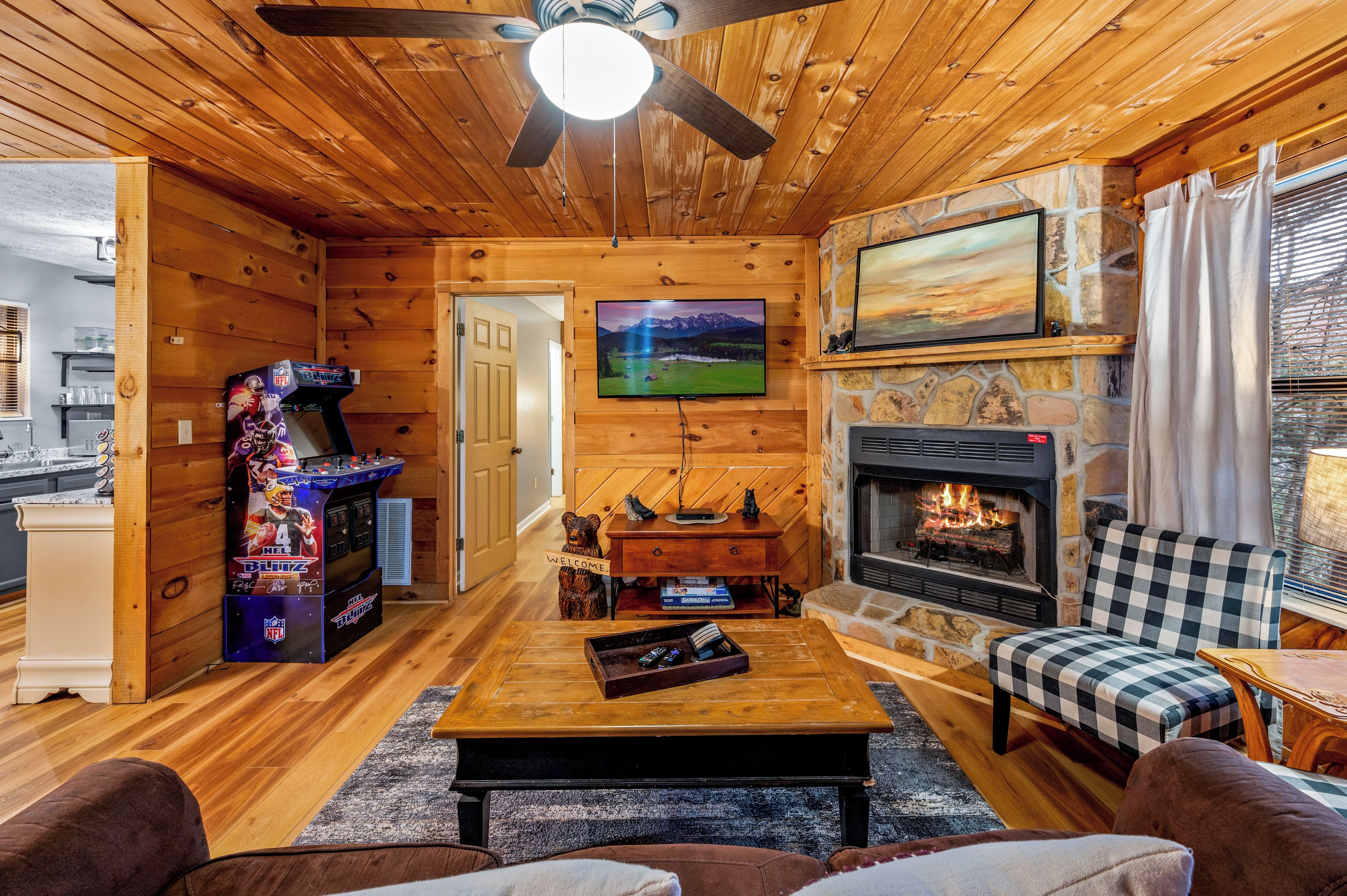 Ein gemütliches Blockhaus-Interieur mit Kamin, einem darüber montierten Fernseher und einem Deckenventilator aus Holz.