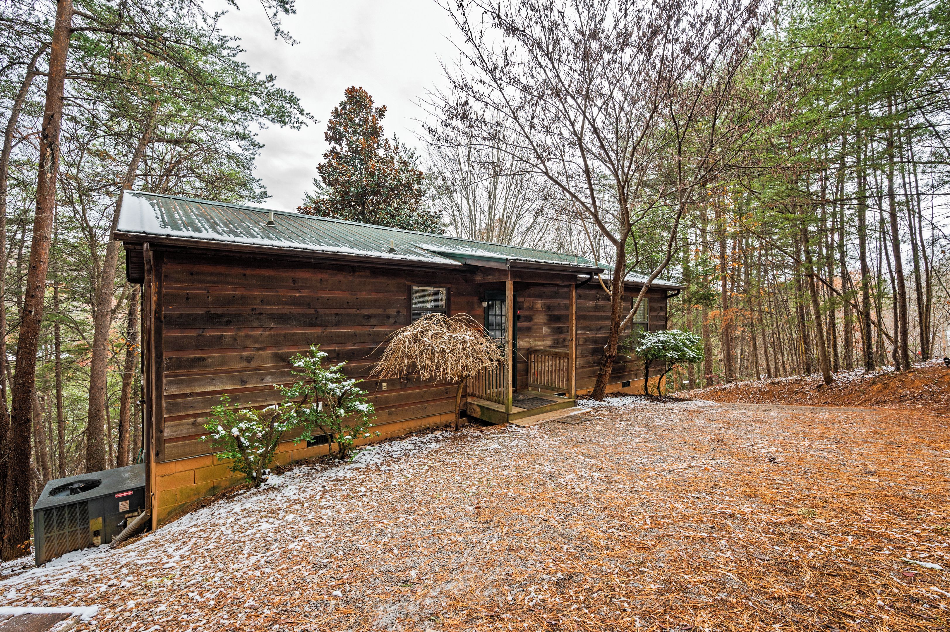 Een houten chalet met een metalen dak, omringd door bomen en een grindpad.