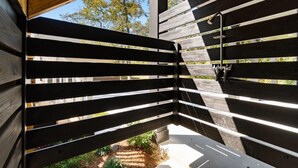 Eine Holzterrasse mit horizontalen Lamellen und einem Duschbereich mit einem Metallarmaturen.