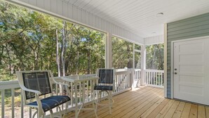 Eine überdachte Veranda mit weißen Geländern und Holzboden, mit zwei weißen Stühlen mit schwarzen Kissen und einem kleinen Tisch.