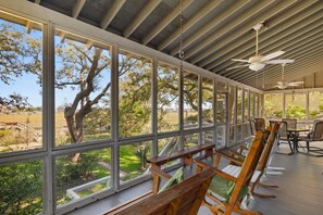 A covered outdoor seating area with wooden benches and tables, large windows, and ceiling fans.
