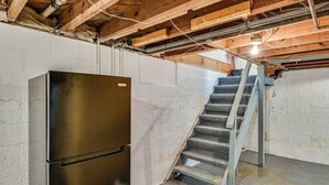 Un sótano con un refrigerador de acero inoxidable, una escalera de concreto y vigas de madera a la vista.