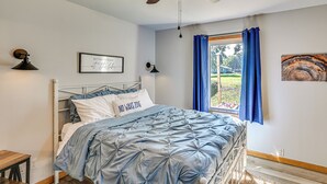Un dormitorio con cama, ventilador de techo, ventana con cortinas, lámpara de pared y una cita enmarcada en la pared.