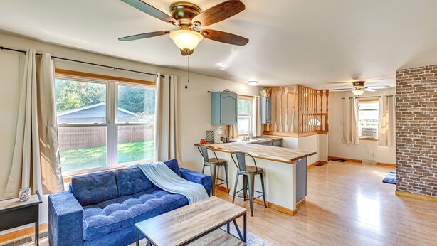 Amplia sala de estar con un sofá azul, una mesa de centro de madera y una cocina con barra y taburetes.