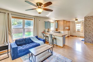 Amplia sala de estar con un sofá azul, una mesa de centro de madera y una cocina con barra y taburetes.
