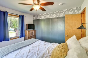 Un dormitorio con cama, ventilador de techo, armario, televisión y ventana con cortinas.