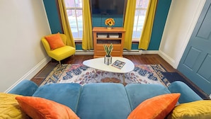 Ein Wohnzimmer mit einem blauen Sofa, einem gelben Sessel und einem Couchtisch mit einer Zeitschrift und einer Pflanze.