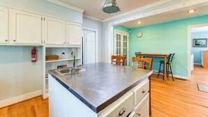 A kitchen with white cabinets, a stainless steel island, and a wooden dining table with chairs. - Spacious New Bern Home w/ Yard: 2 Mi to Riverfront (New Bern)