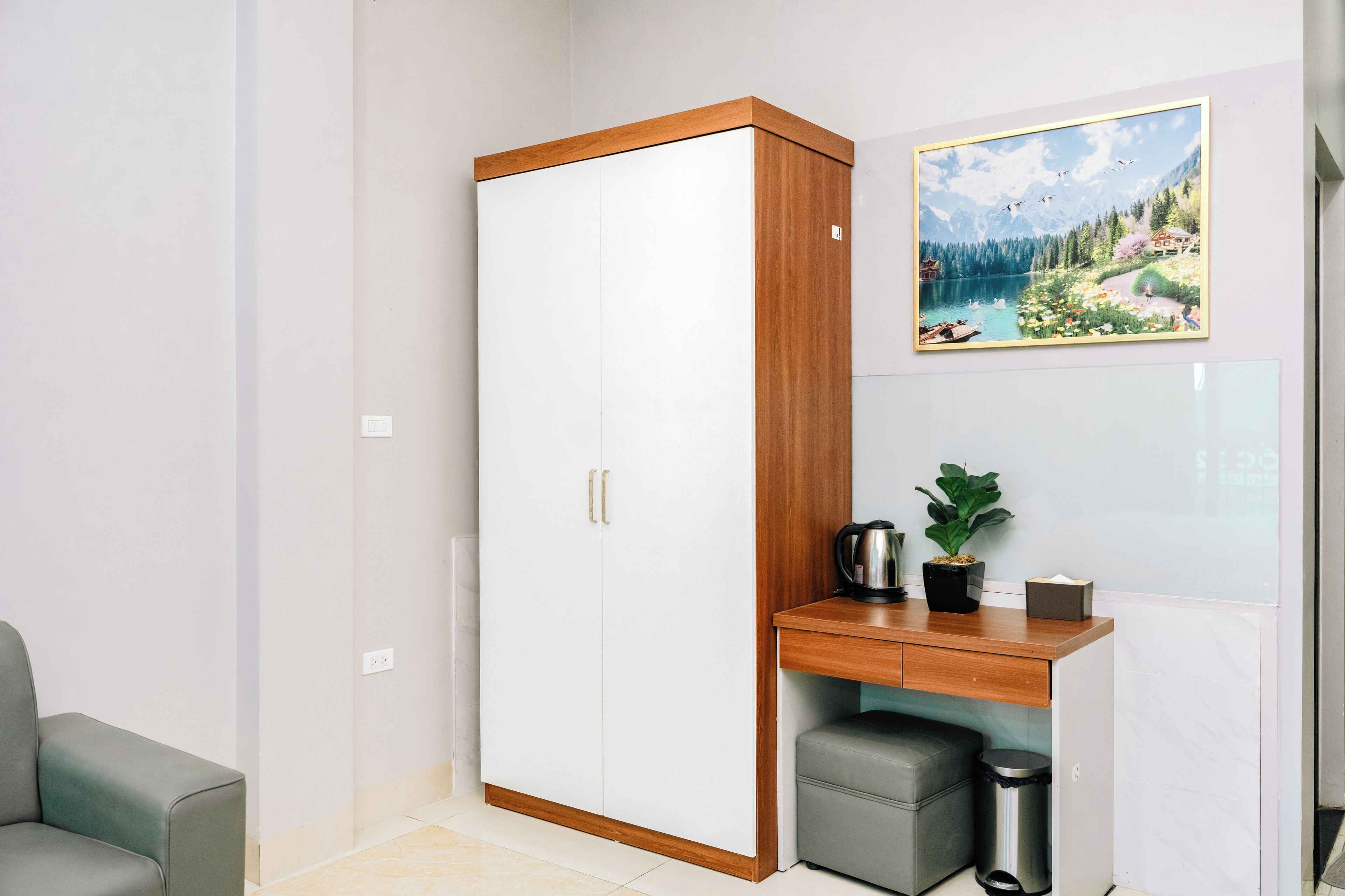 Quarto com armário, uma pequena escrivaninha com uma planta, chaleira e lixeira.