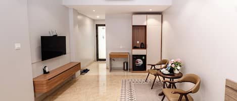 Une chambre d’hôtel moderne équipée d’un téléviseur à écran plat, d’un banc en bois, d’un coin repas avec des chaises, d’une petite table et d’un tapis à motifs.