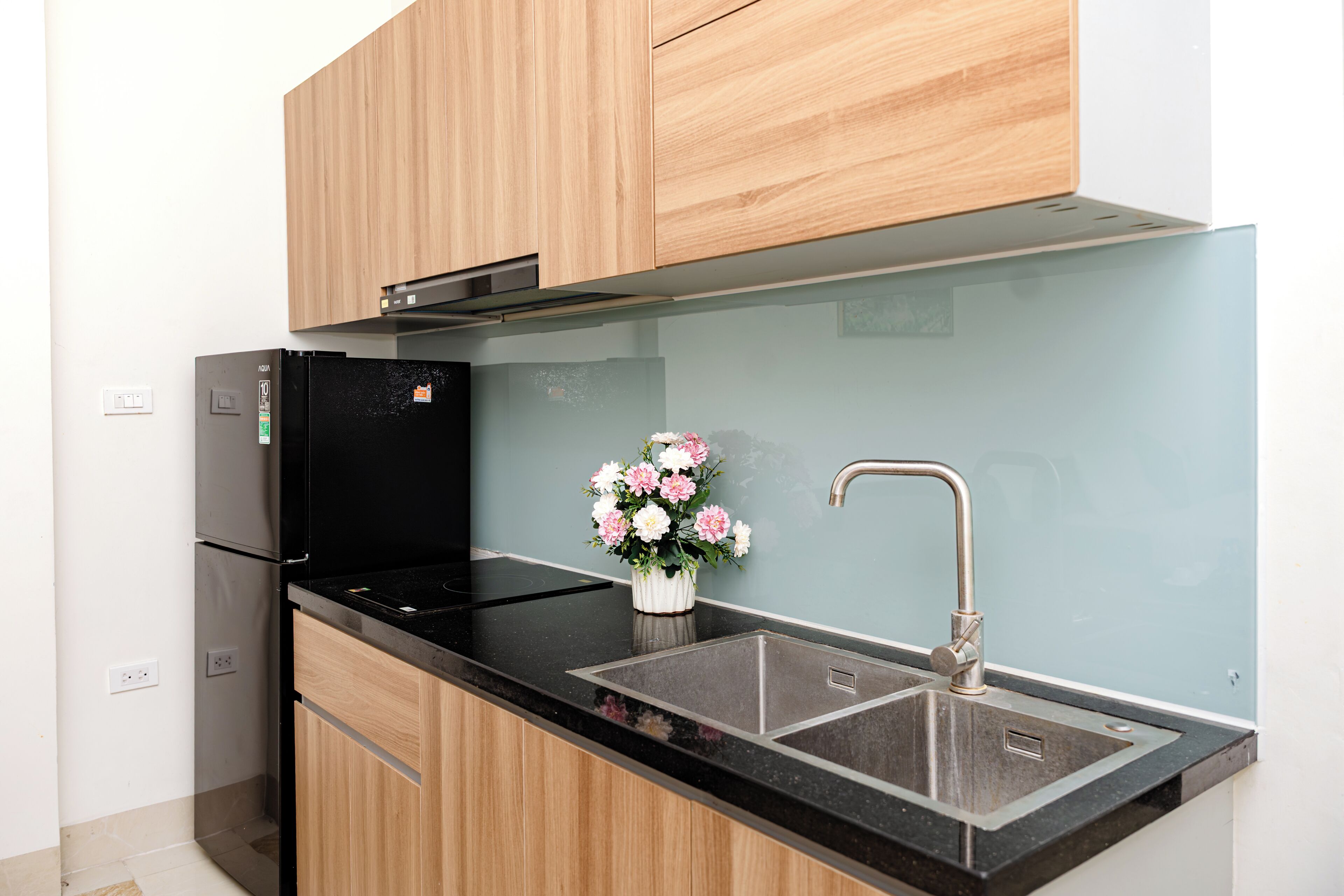 A modern kitchen with a black refrigerator, wooden cabinets, a stainless steel sink, and a vase with flowers.