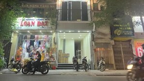 A multi-story building with illuminated windows and balconies, surrounded by shops and parked motorcycles. - Hoang Long Apartment (Hanoi)
