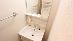Un baño pequeño con lavamanos, espejo, baranda y dispensador de jabón.
