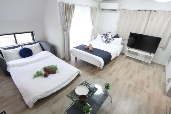 A modern hotel room with two beds, a flat-screen TV, a glass coffee table, and a small potted plant.