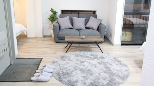 Una sala de estar con un sofá gris, una mesa de centro de madera, un tapete espeso grisáceo y una planta pequeña.